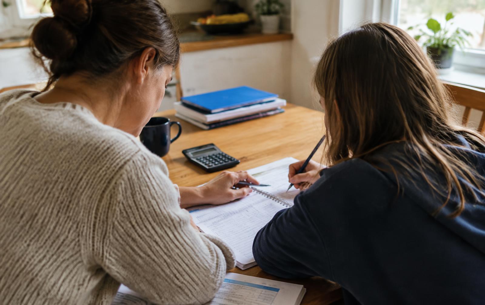 Mãe ajudando o filho com a lição de casa em uma mesa com cadernos, calculadora e documentos